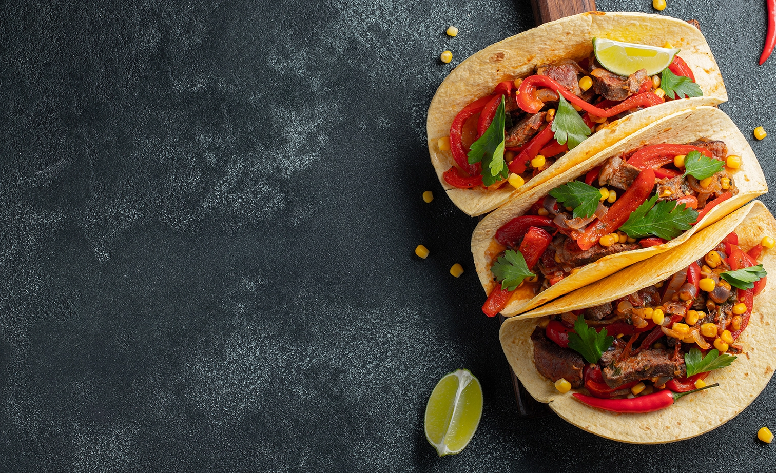 Three loaded tacos with peppers, corn, and lime.