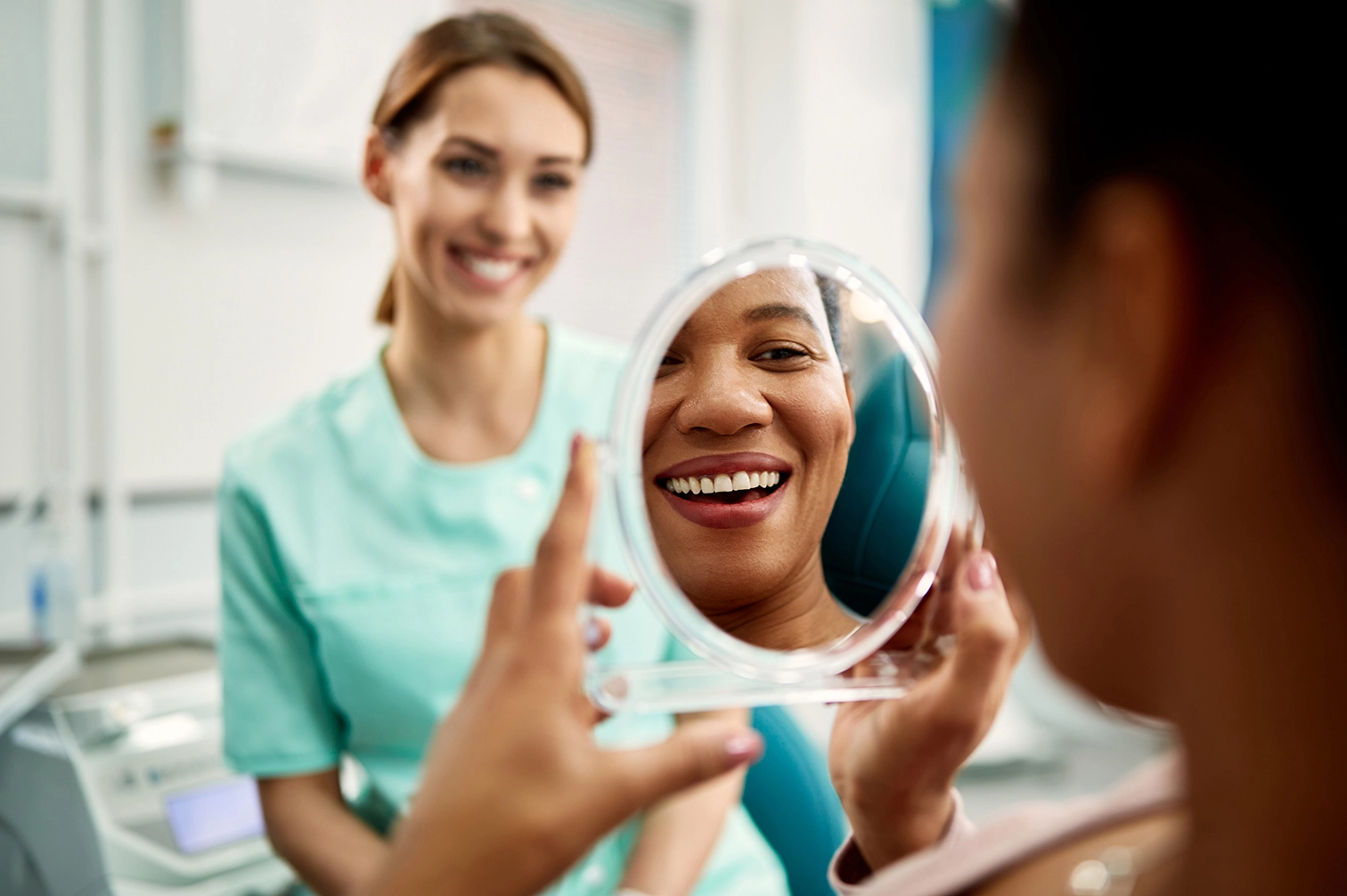 Patient smiling into a handheld mirror at the dentist.