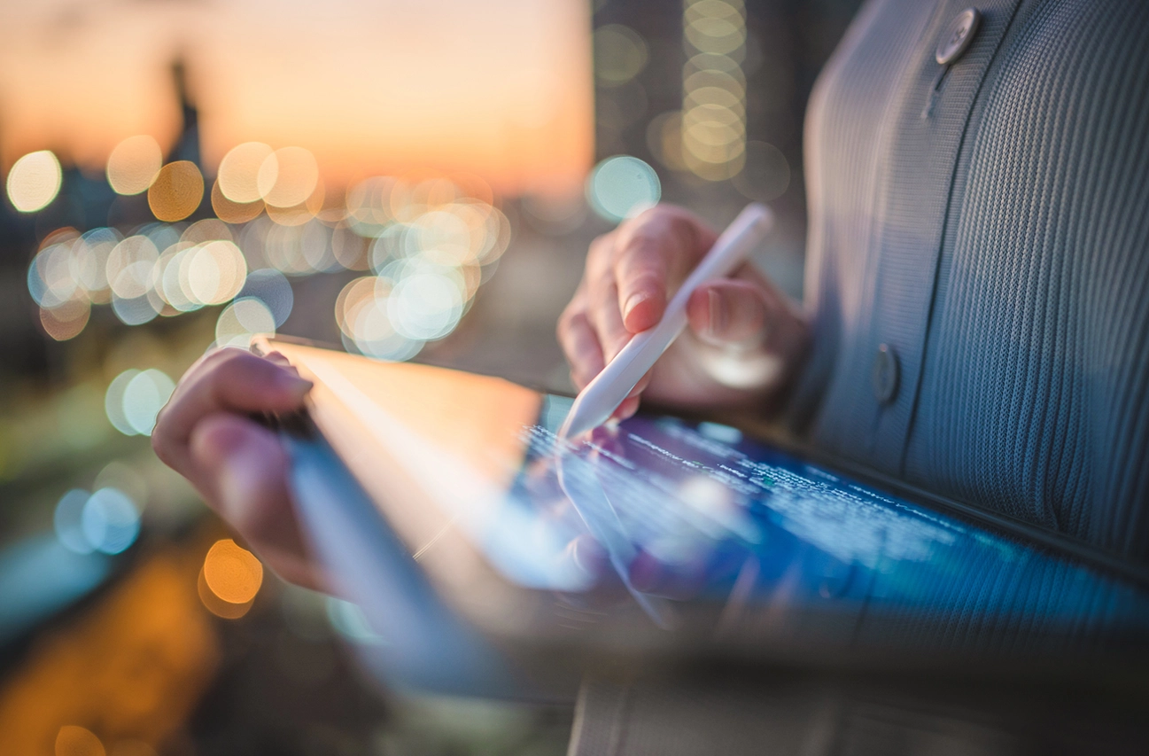 Person writing on a tablet with a stylus at dusk.