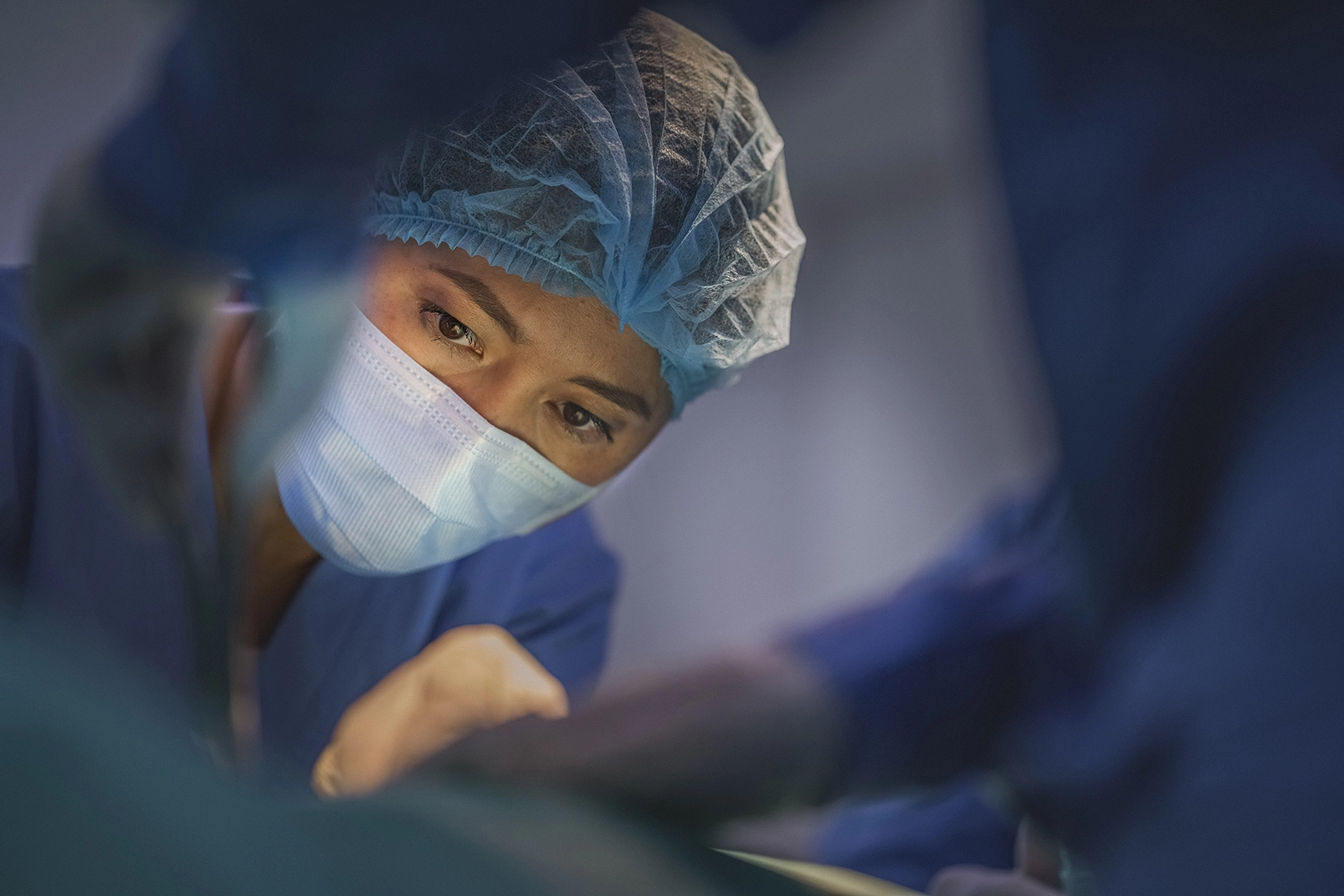 Surgeon in mask and cap focused during an operation.